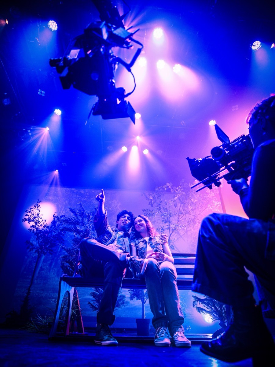 Two AMDA acting students filming a scene on a bench under blue stage lights, with cameras rolling