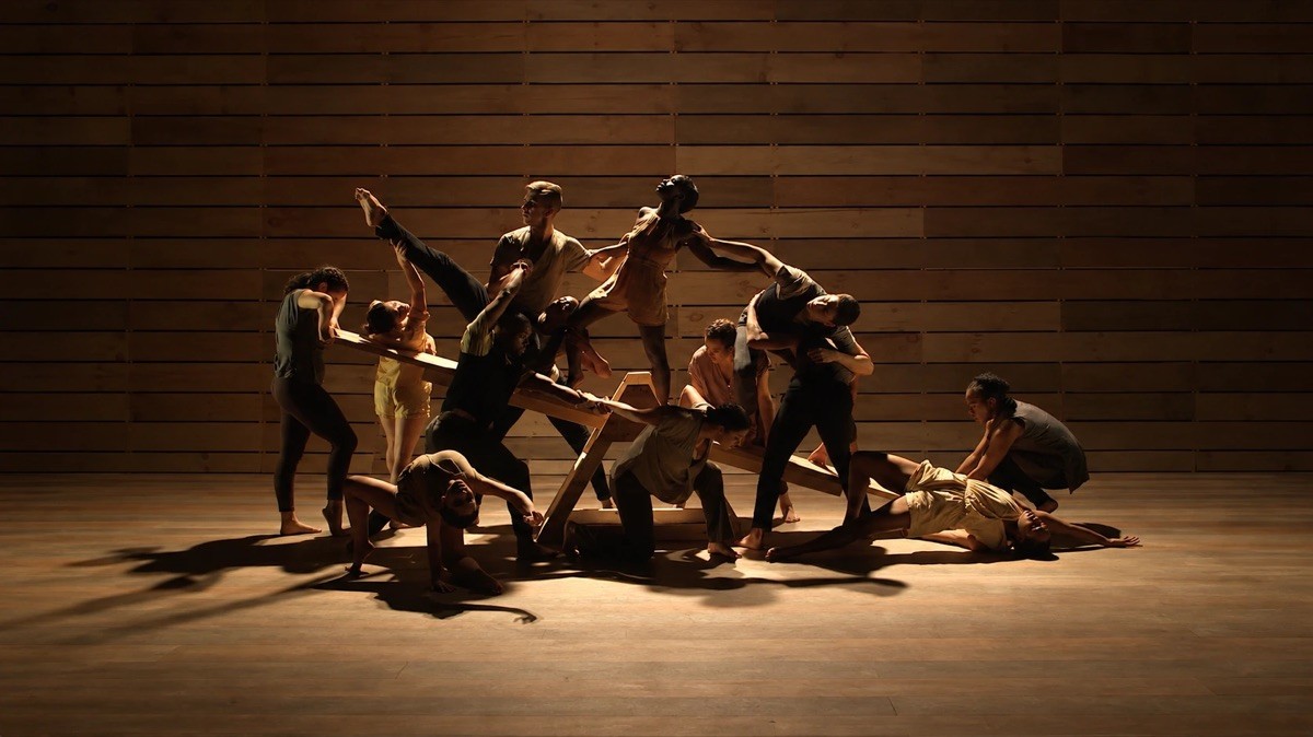 AMDA dancers in warm stage light arranged around a wooden seesaw